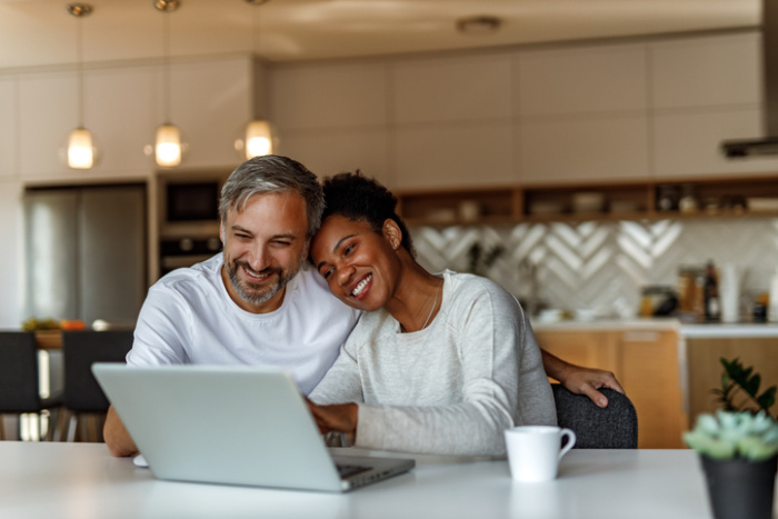 A couple sitting at a table looking on laptop together and smiling