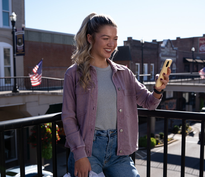 Girl holding shopping bags outside looking at phone and smiling