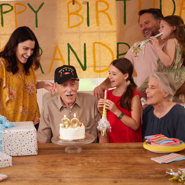 Grandpa blowing out 90th birthday candles, surrounded by family.